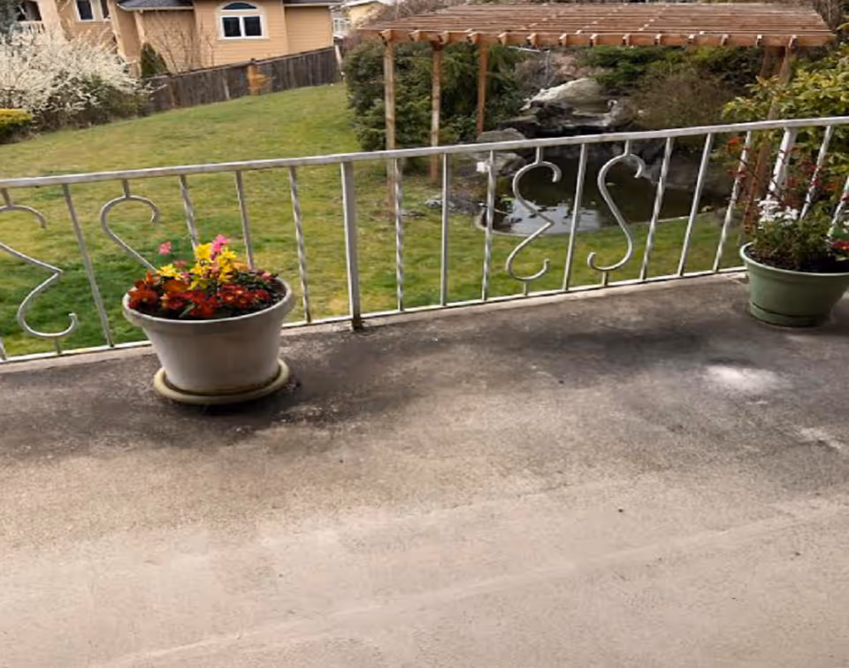 Balcony railing with flower pots overlooking a grassy yard and pergola.