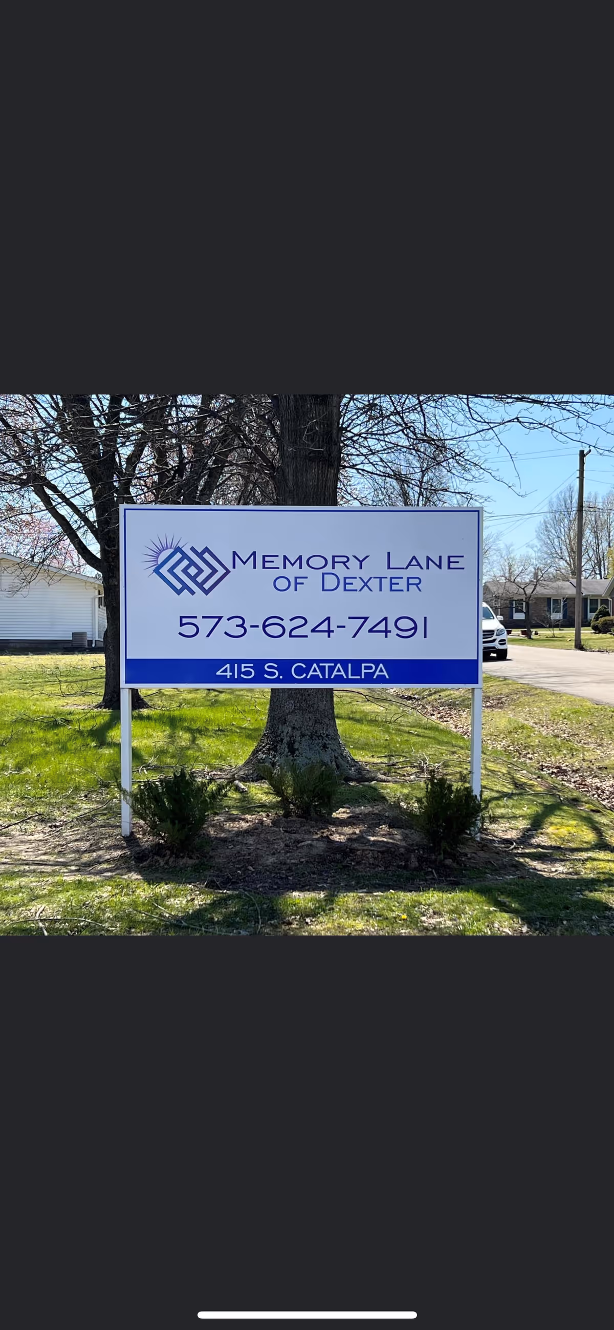 Outdoor scene showing Memory Lane of Dexter sign with landscaping and surrounding houses.
