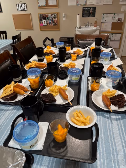 Dining room in a senior facility with meals plated on trays at a long table.