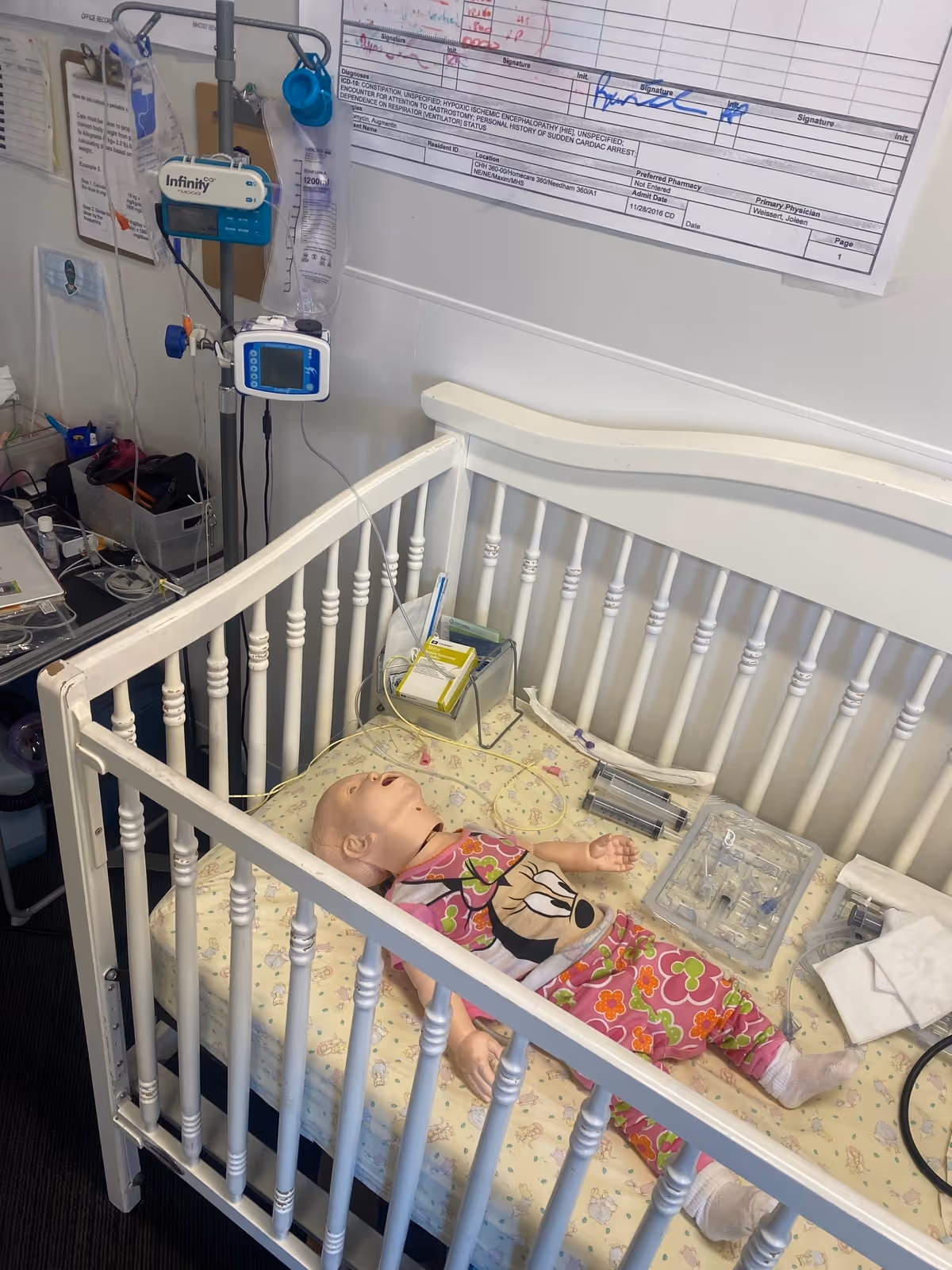 Hospital crib with medical equipment and a doll inside a clinical patient room.