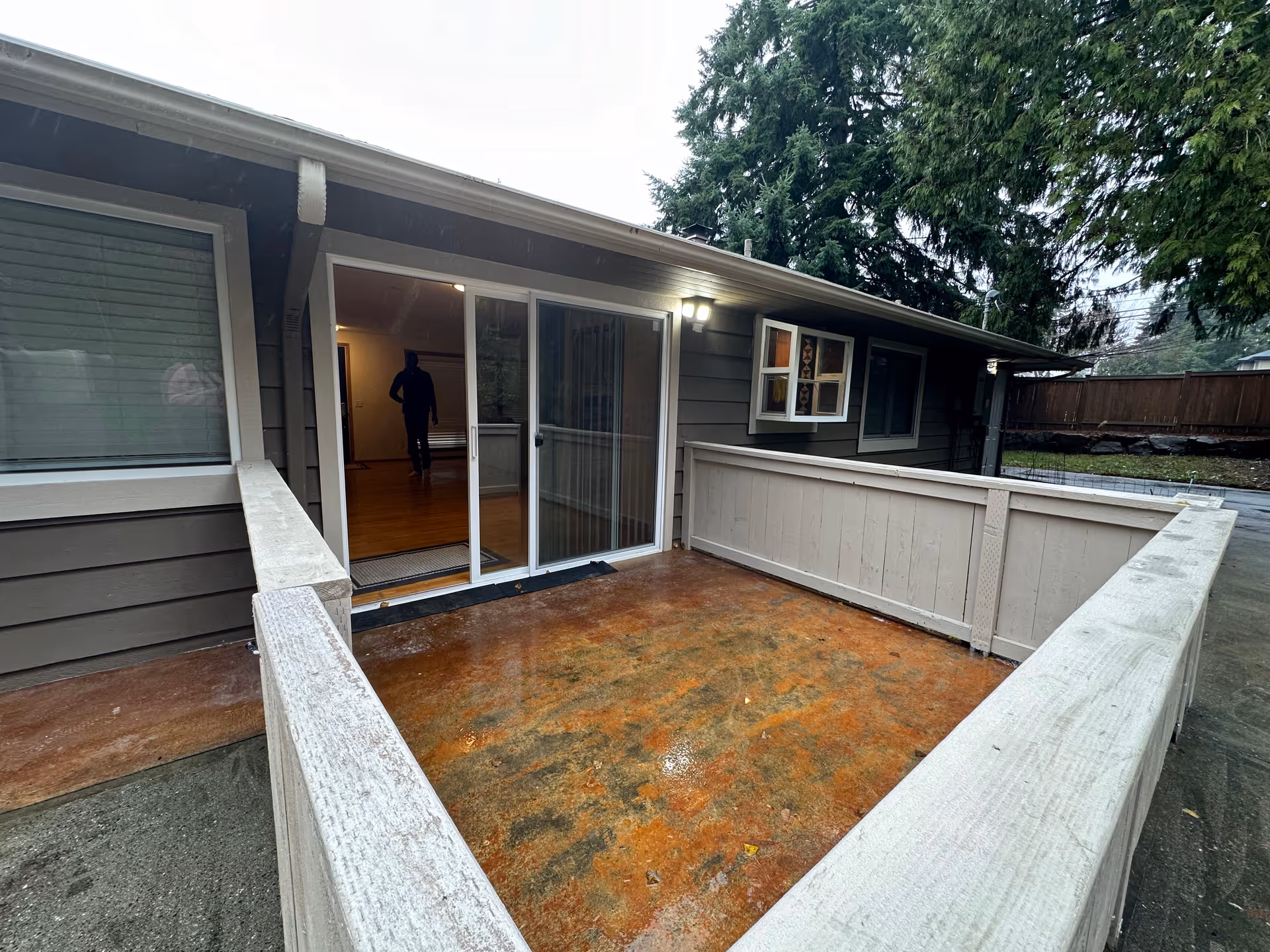 Exterior view of a gray, single-story home with sliding doors and a wooden deck.