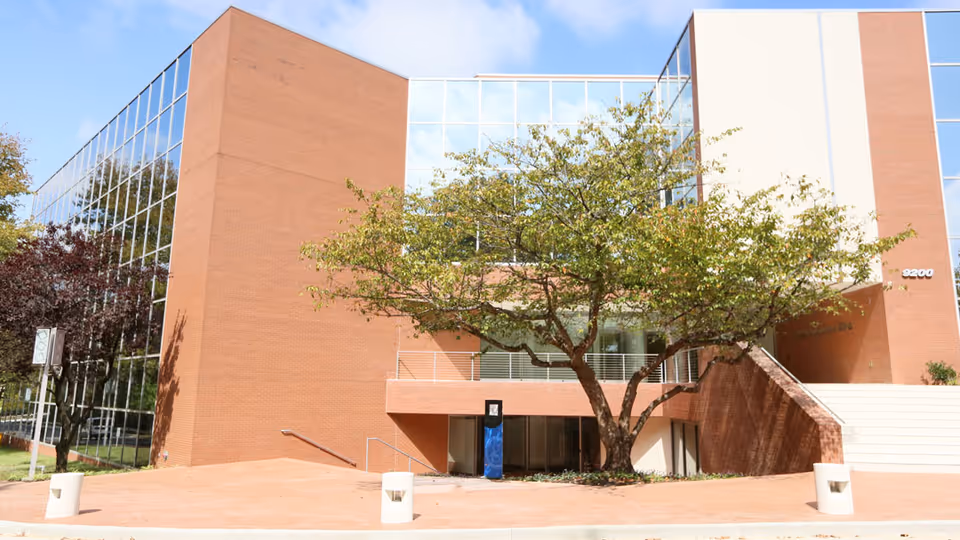 Modern brick and glass building exterior with a tree-lined entrance area.