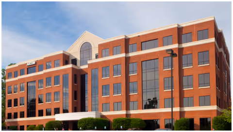 Red brick, multi-story facility with large windows and a glass entrance under blue sky.