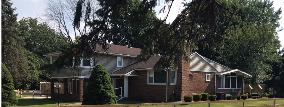 Single-story brick assisted living facility exterior with trees and manicured lawn