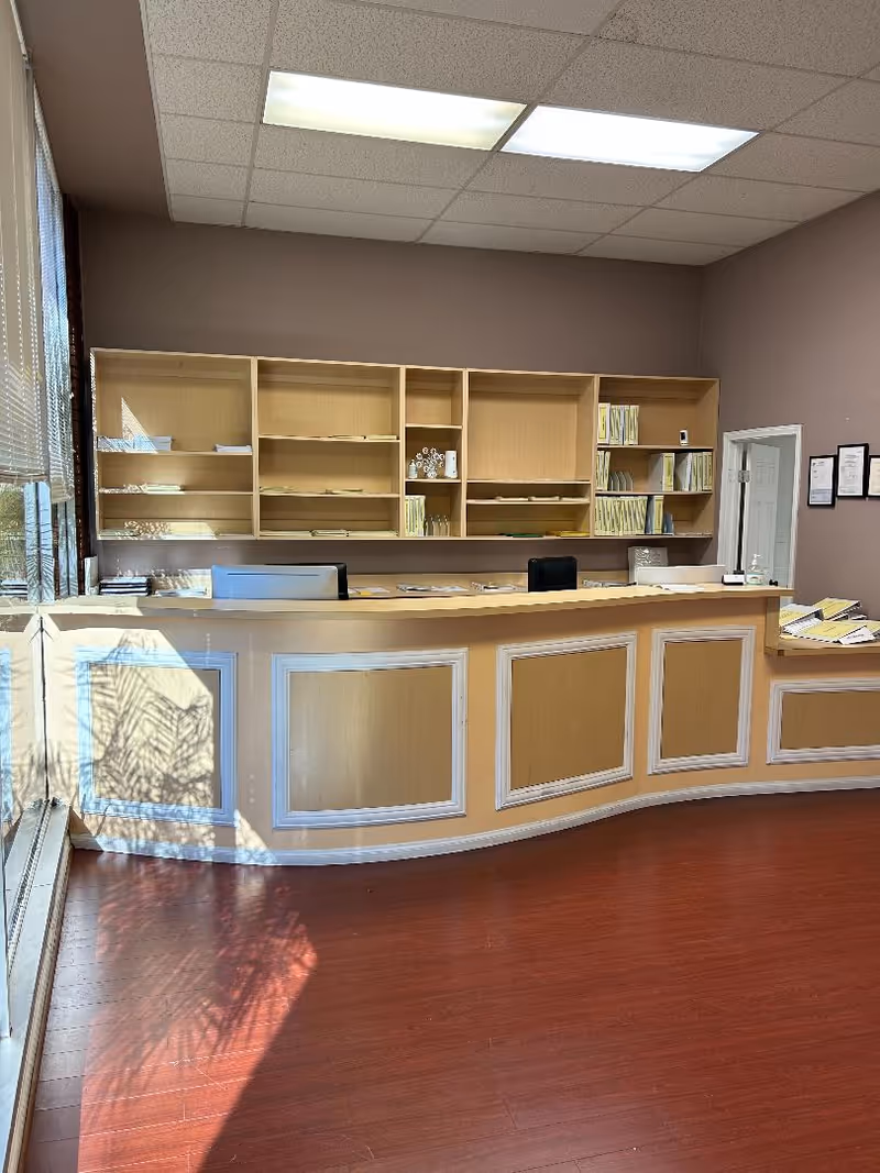 Well-lit reception desk with shelves behind, wooden paneling, and red-toned flooring.