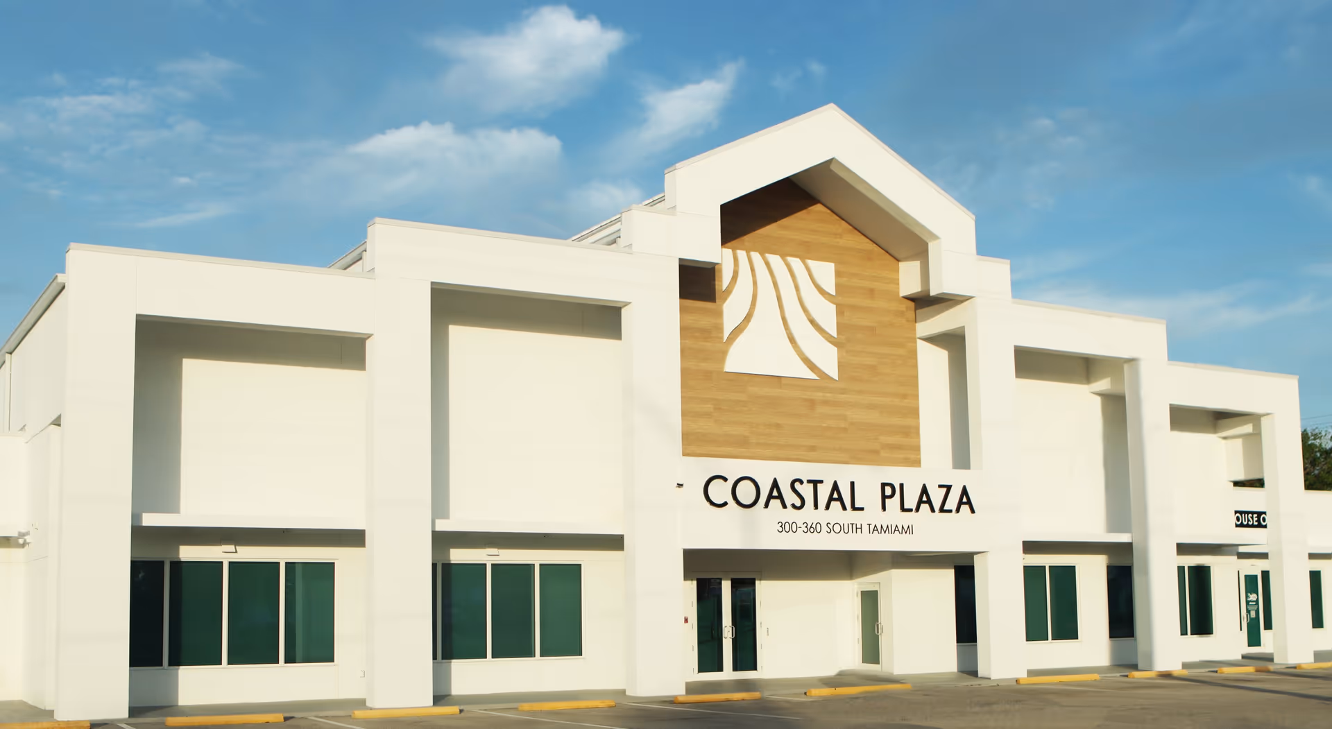 White modern building exterior with Coastal Plaza sign under blue sky.