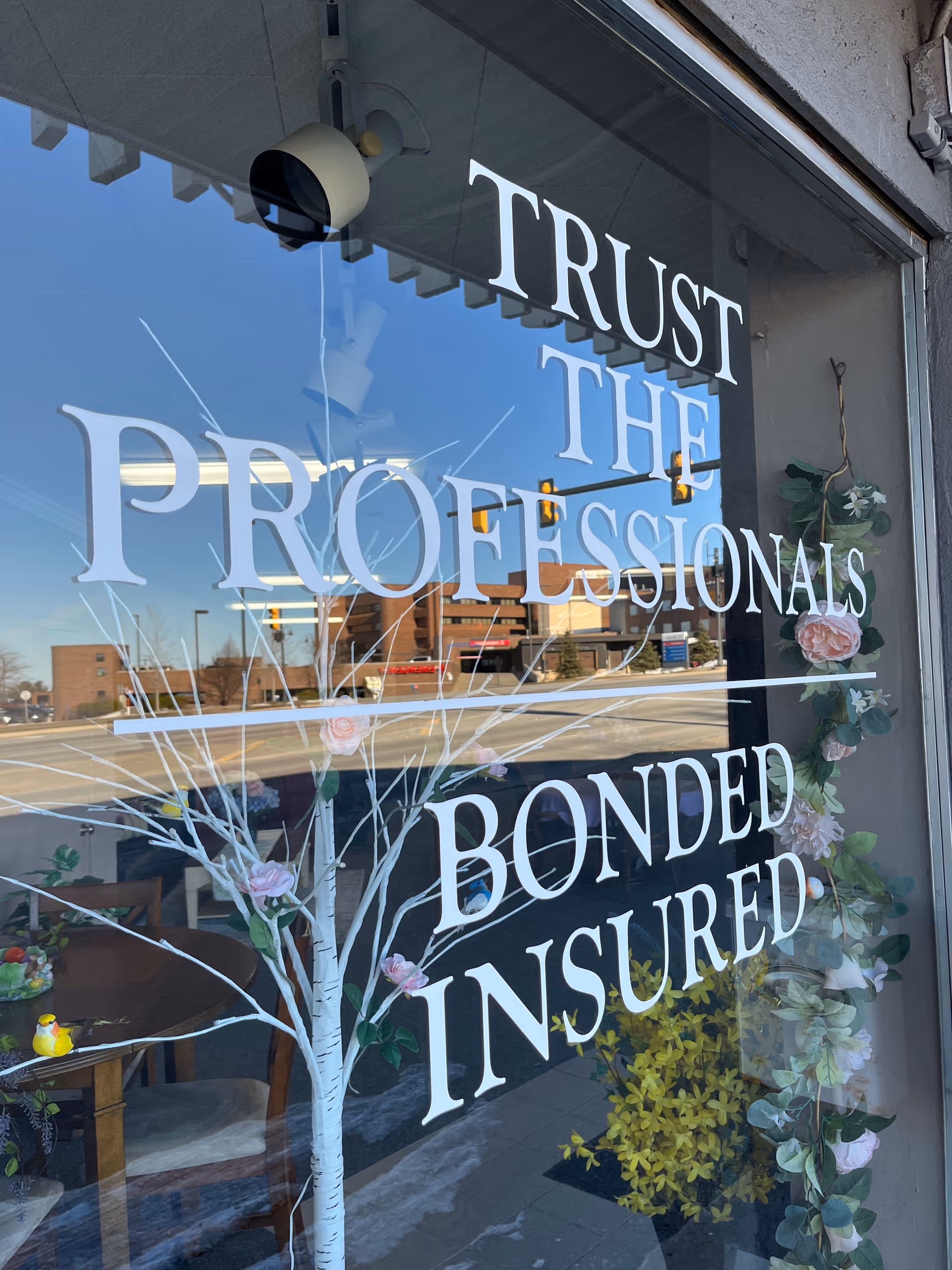 Storefront window displays Trust the Professionals Bonded Insured with floral decor.