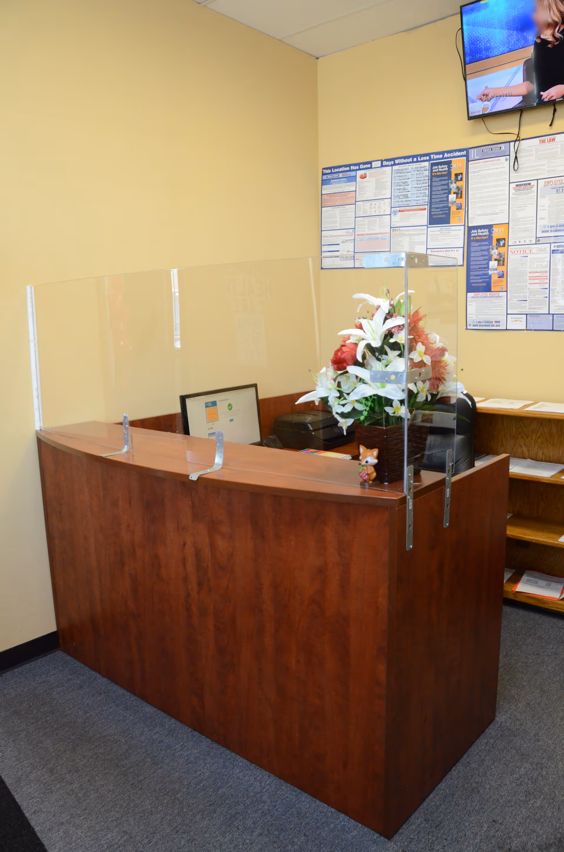 Reception desk with plexiglass dividers inside yellow-walled senior living facility lobby.