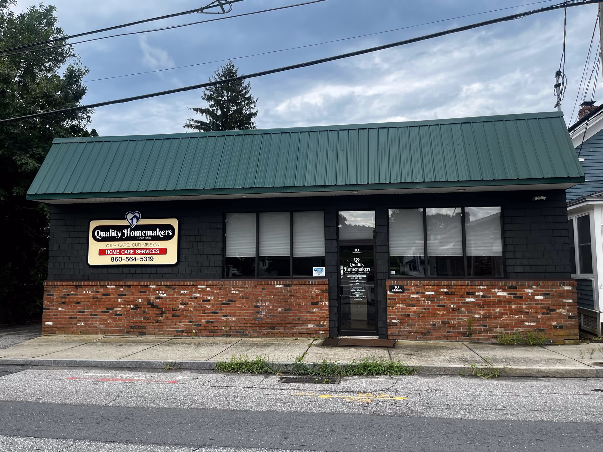 Brick storefront with green roof and a Quality Homemakers sign beside a glass door.