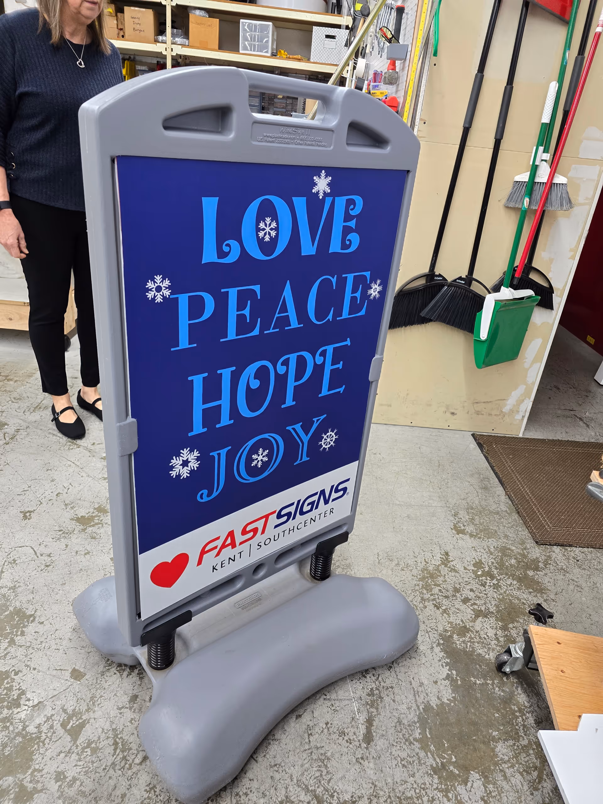 Indoor freestanding sign with LOVE PEACE HOPE JOY and FastSigns logo in a utility area.