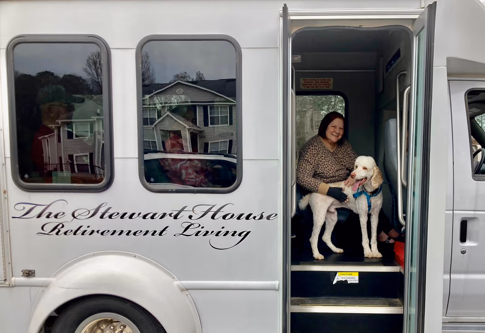 A woman sits with two dogs in the doorway of a Stewart House Retirement Living bus.