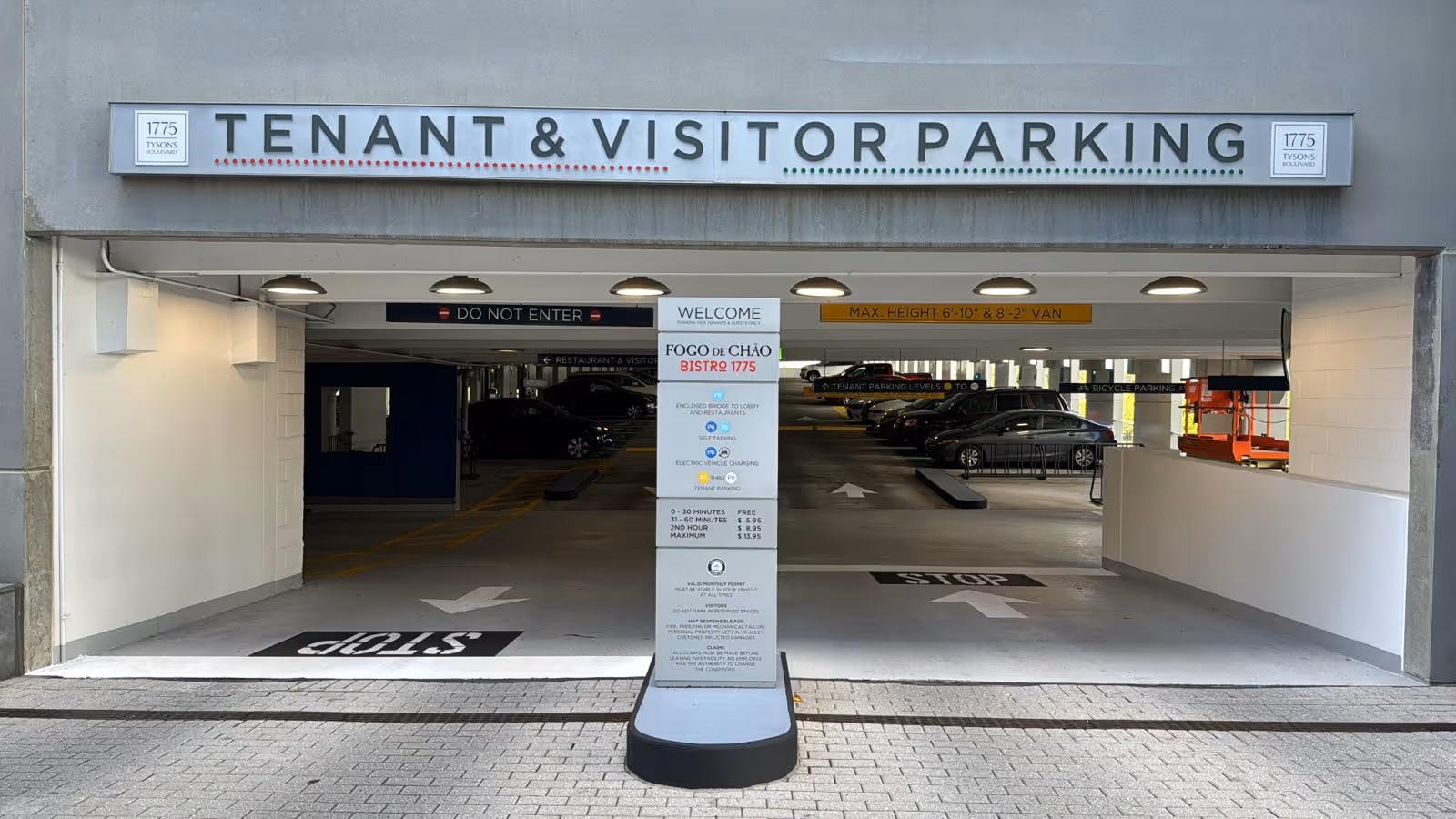 Facade of a parking garage with Tenant and Visitor Parking sign and open entrance.