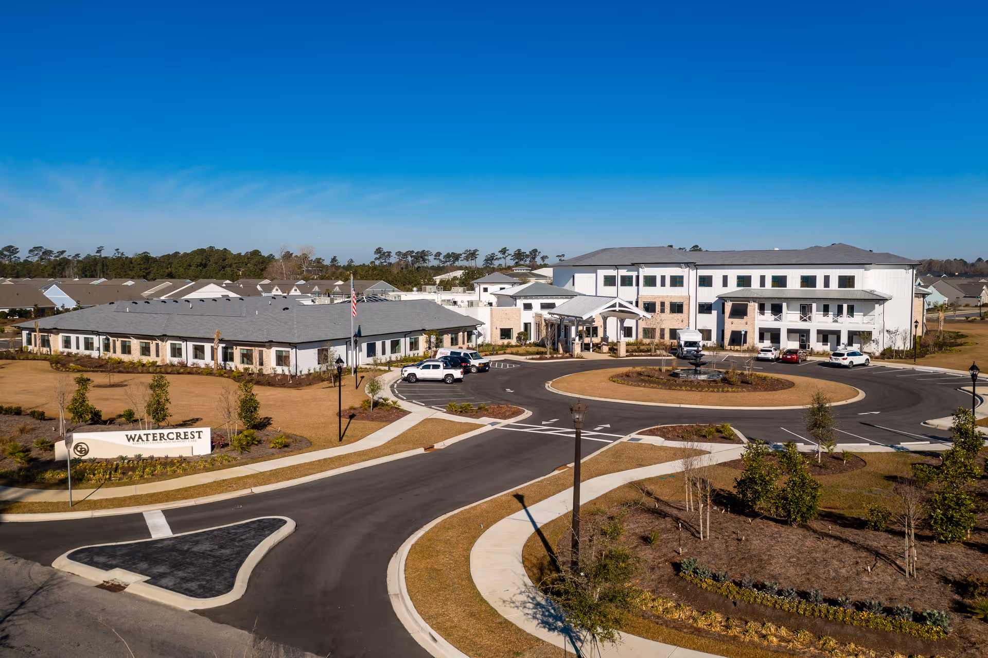 Aerial view of the Watercrest Myrtle Beach senior living campus with buildings, roundabout fountain, parking and landscaped entrance sign.