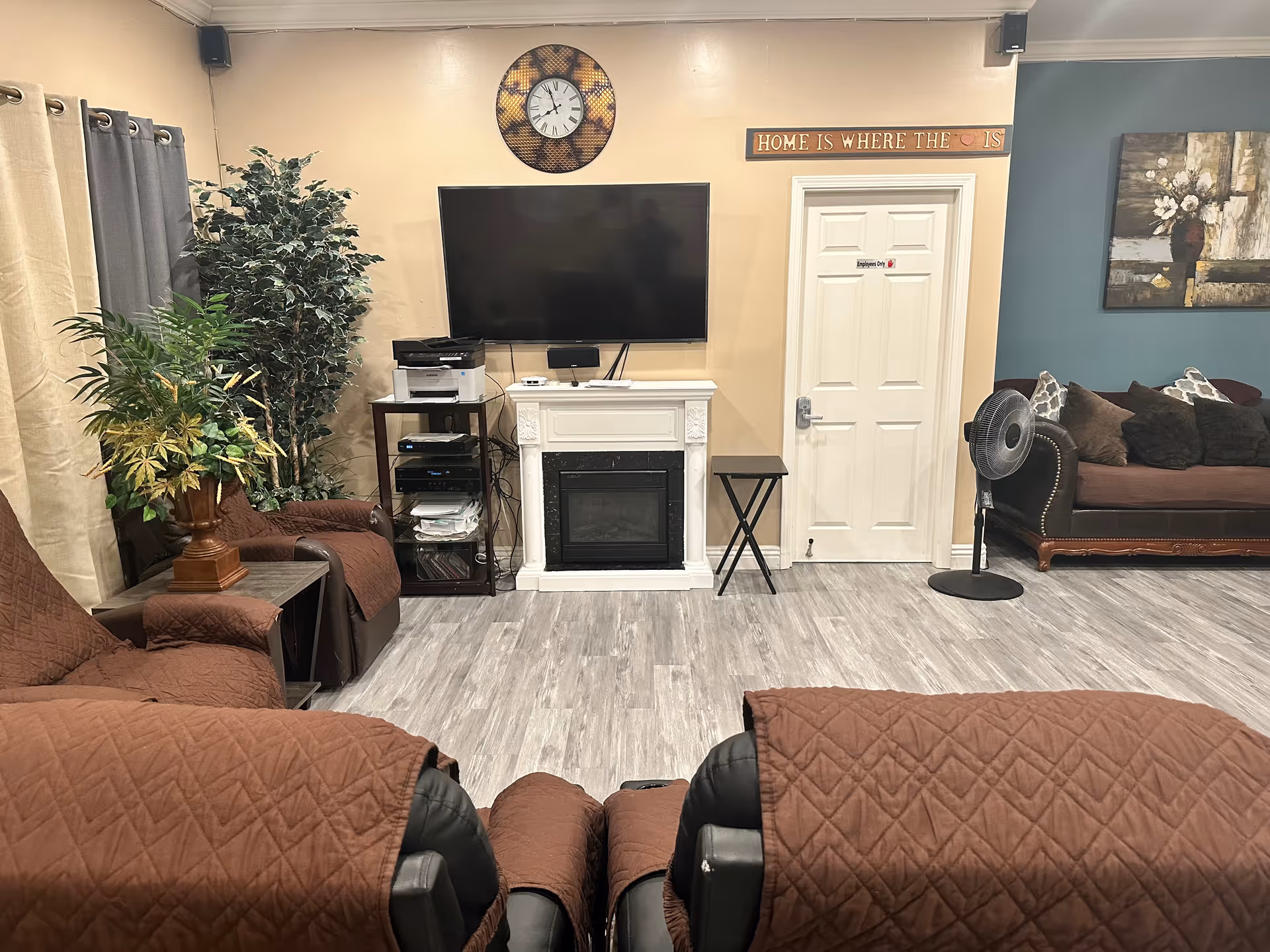 Common living room with brown recliners, sofa, TV, fireplace mantel, plants, and doorway.