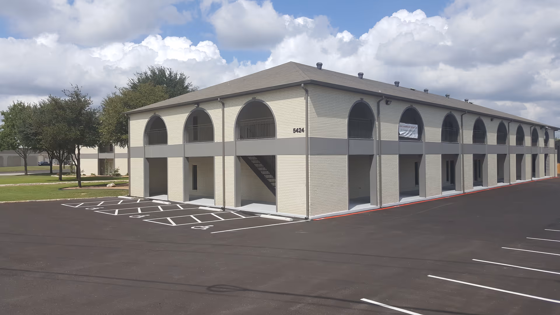 Two-story beige senior living building with arched windows and a large parking lot.