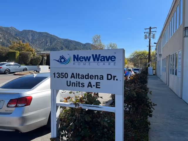 Outdoor view of New Wave Home Care sign with parked cars beside the building.