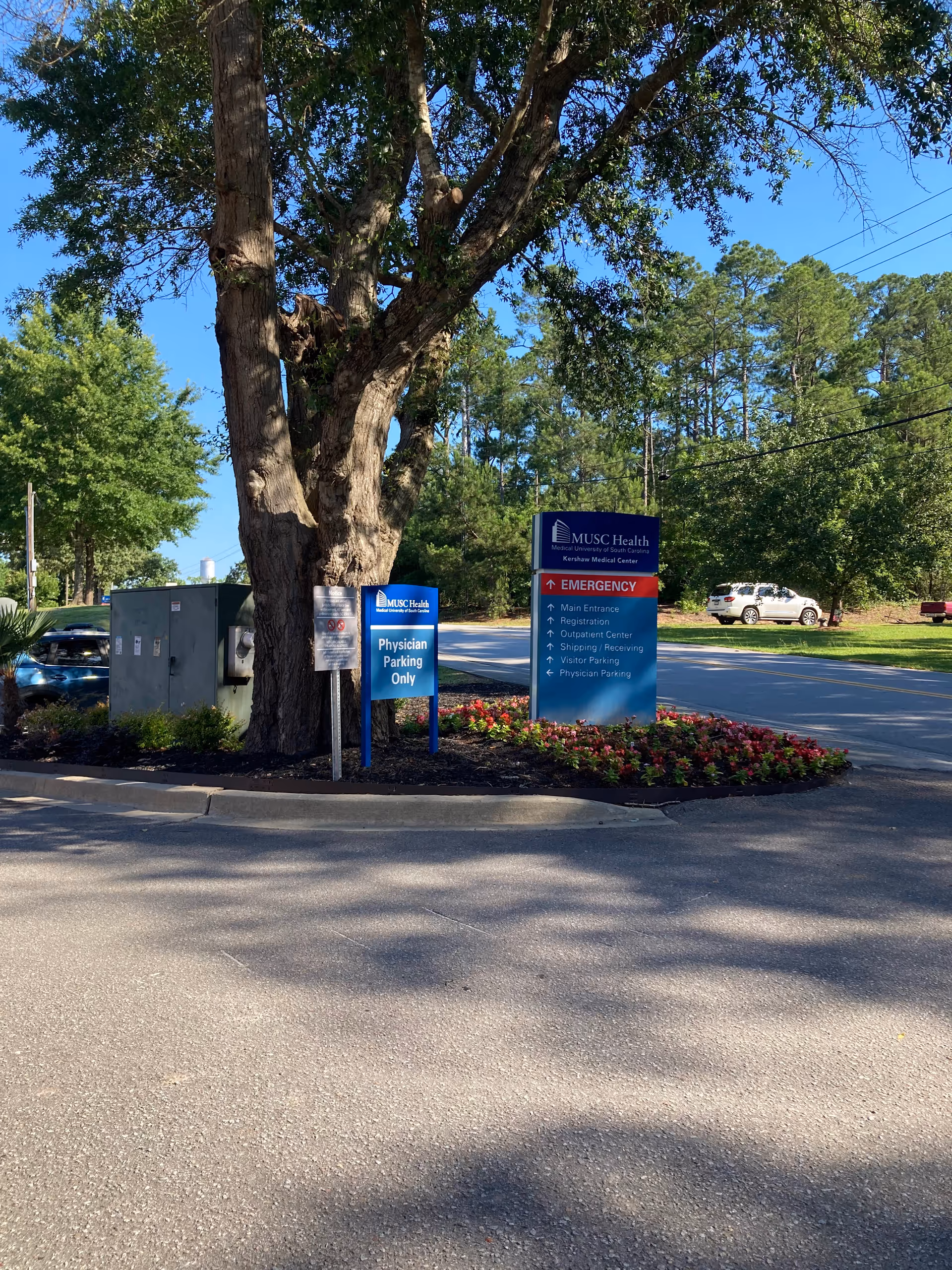 Parking area and front signs for MUSC Health Kershaw Medical Center near trees.