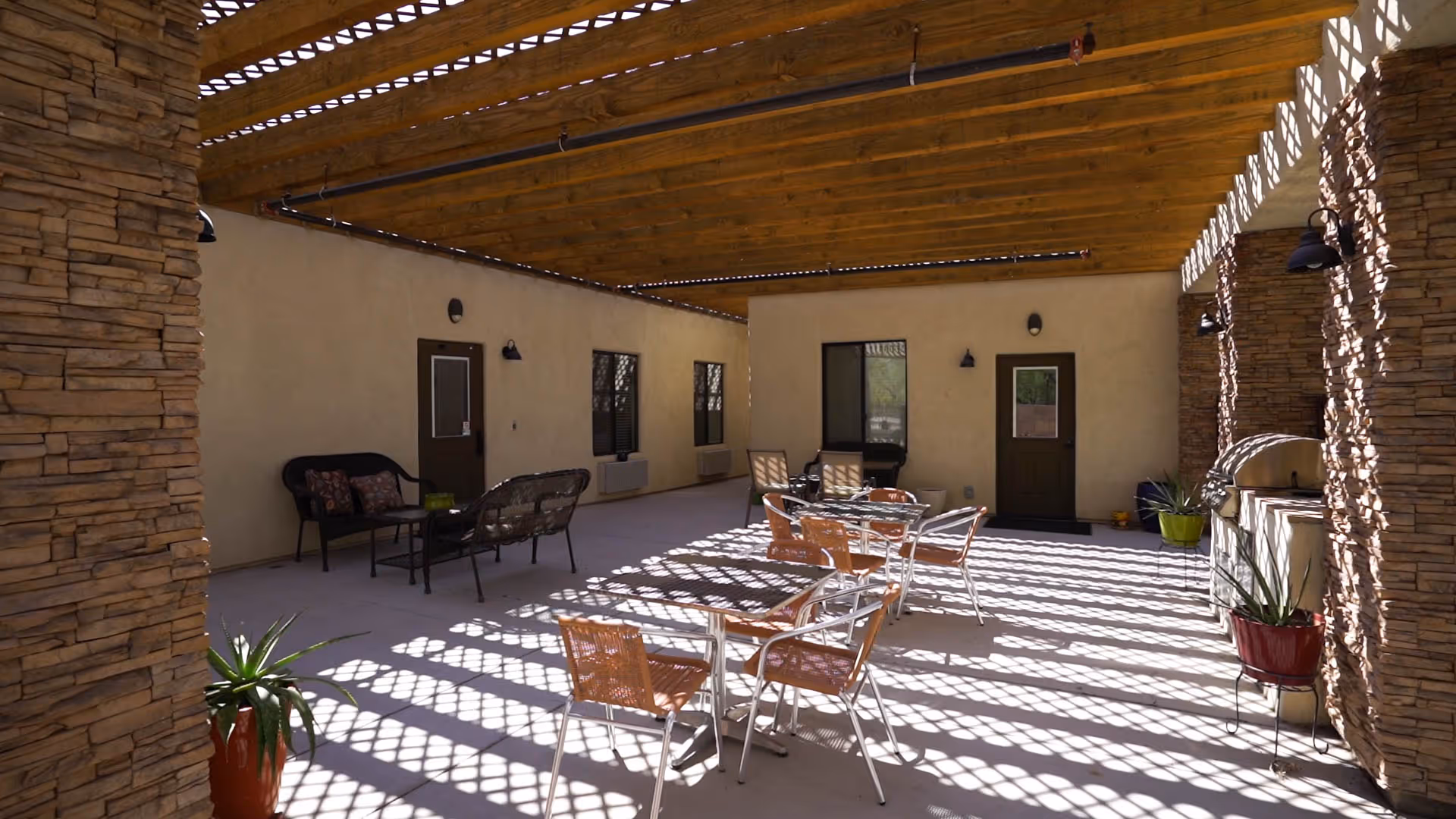 Shaded outdoor patio at BeeHive Homes of Marana with tables, chairs, and stone columns.