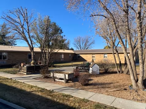 Exterior of Elder Inn senior living facility with courtyard, benches, trees, and gravel landscaping.