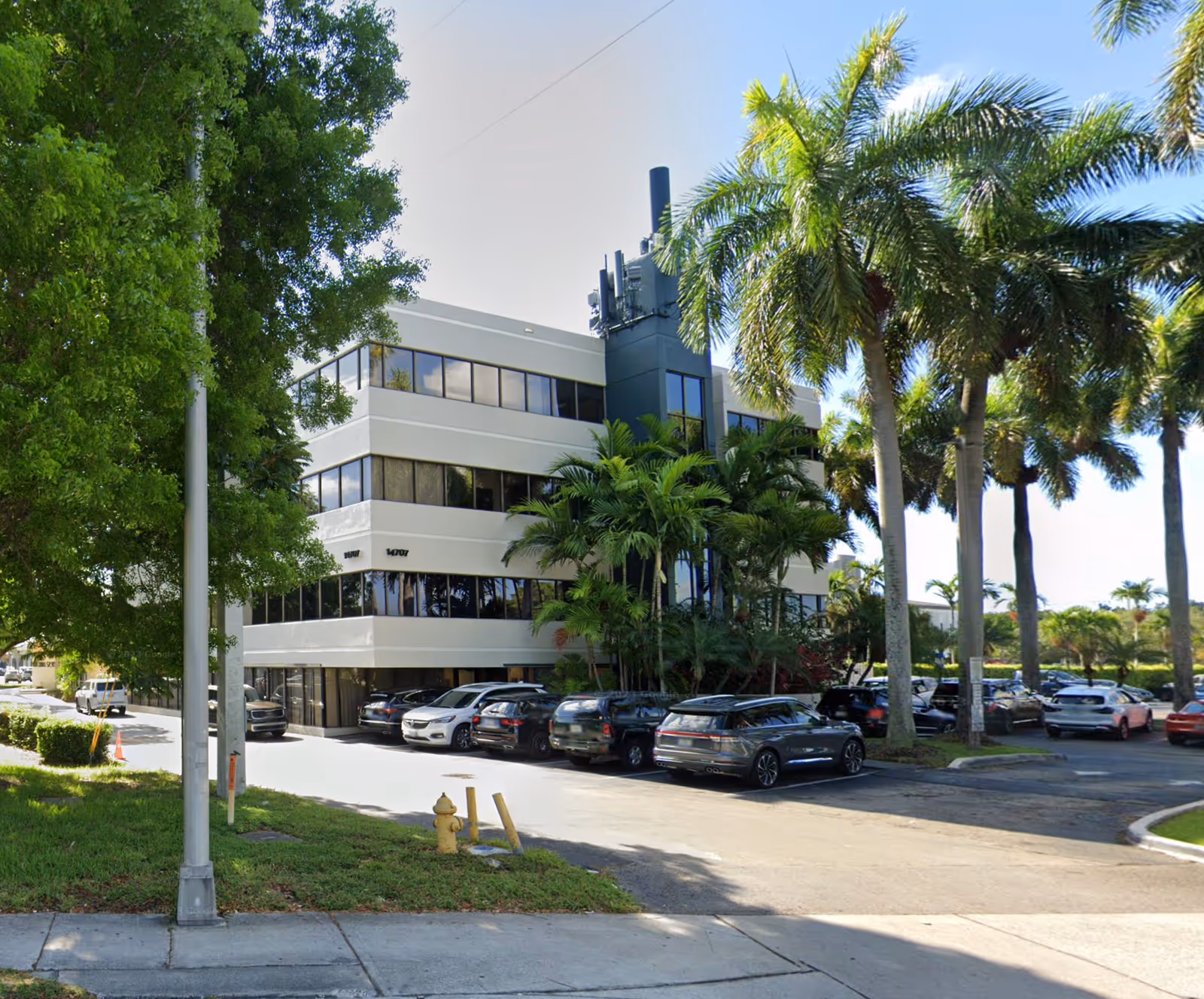 Exterior of a modern, multi-story building with a parking lot and palm trees