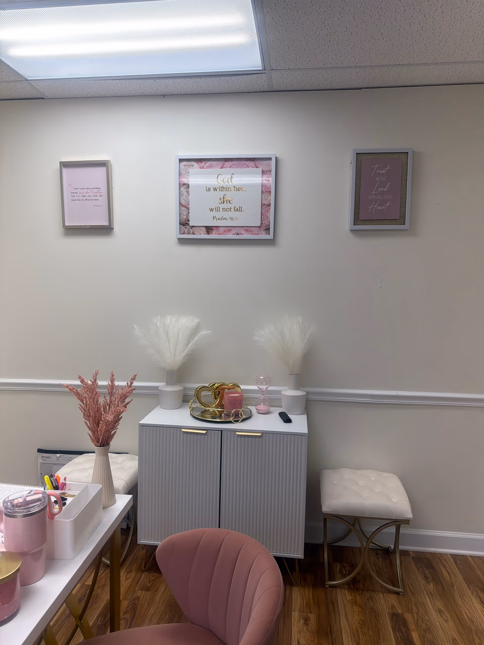 Pastel-themed interior room with pink seating, decorative vases, framed wall art, and a cabinet.