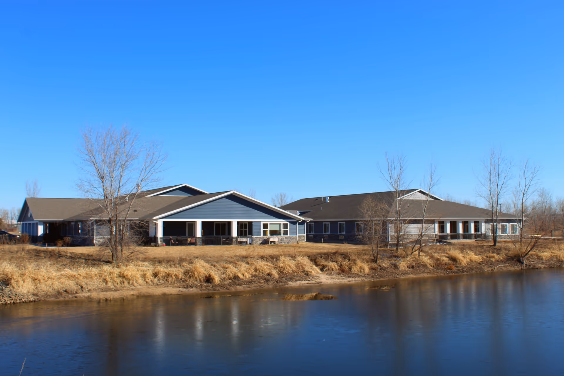 Exterior view of BeeHive Homes of Eau Claire along a riverbank with blue siding.