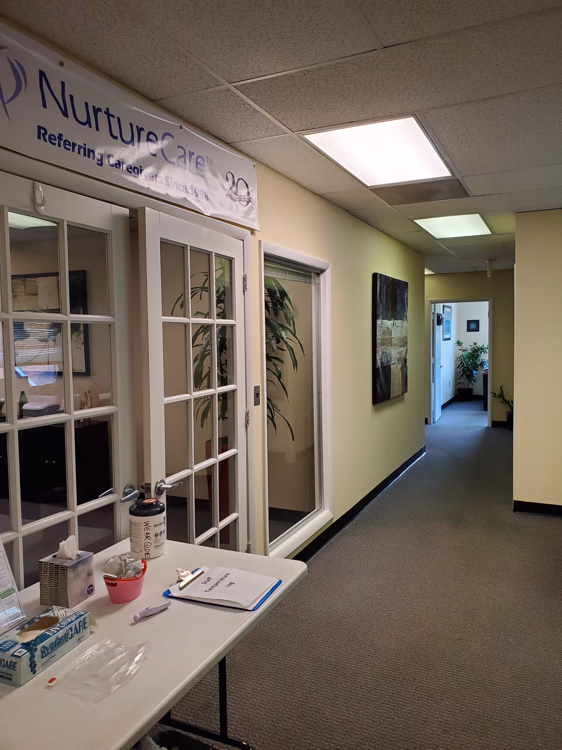 Indoor hallway featuring a NurtureCare banner, glass doors, and a table with medical supplies.
