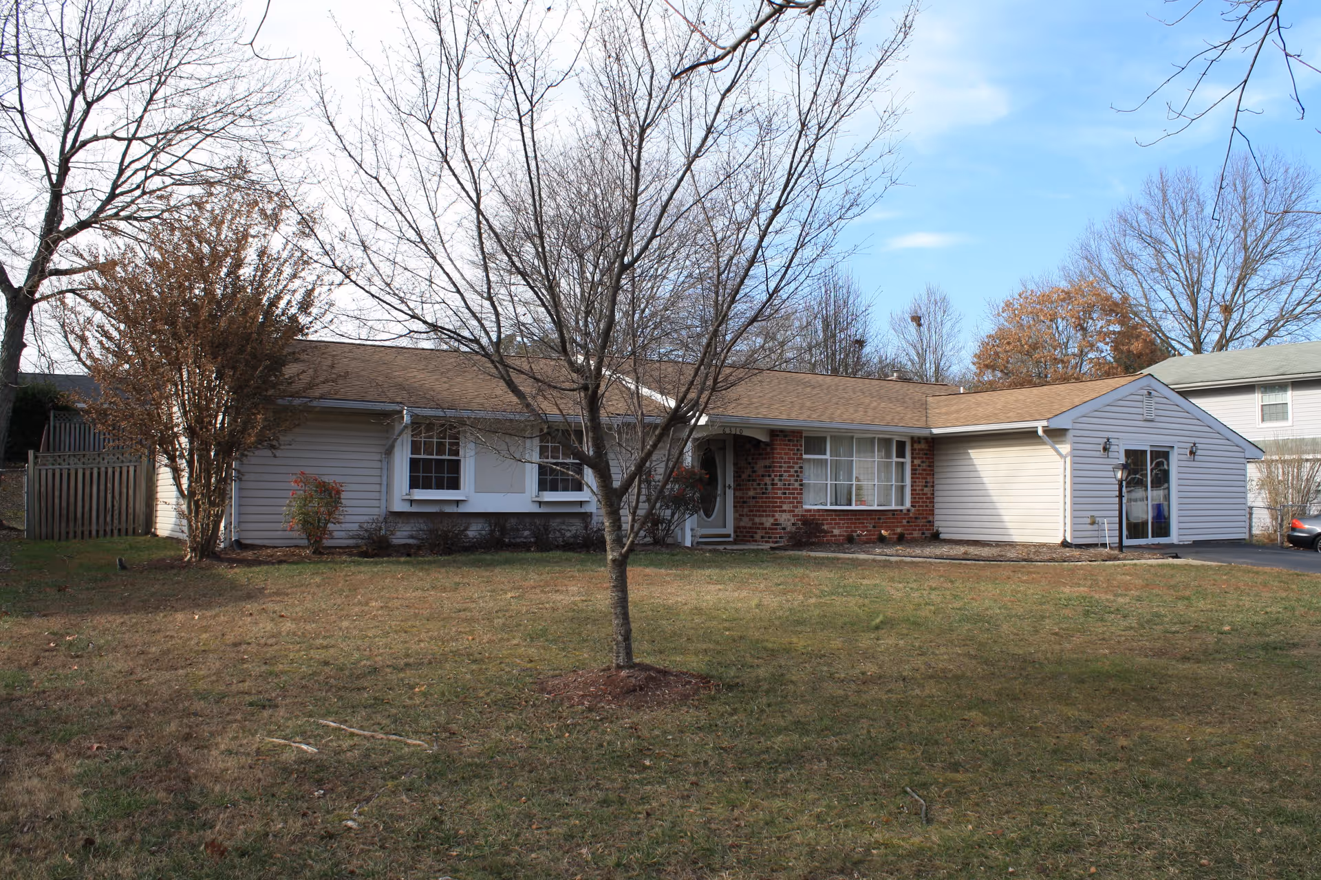 Single-story ranch-style building with a front lawn, a leafless tree, and an attached garage under a clear sky.