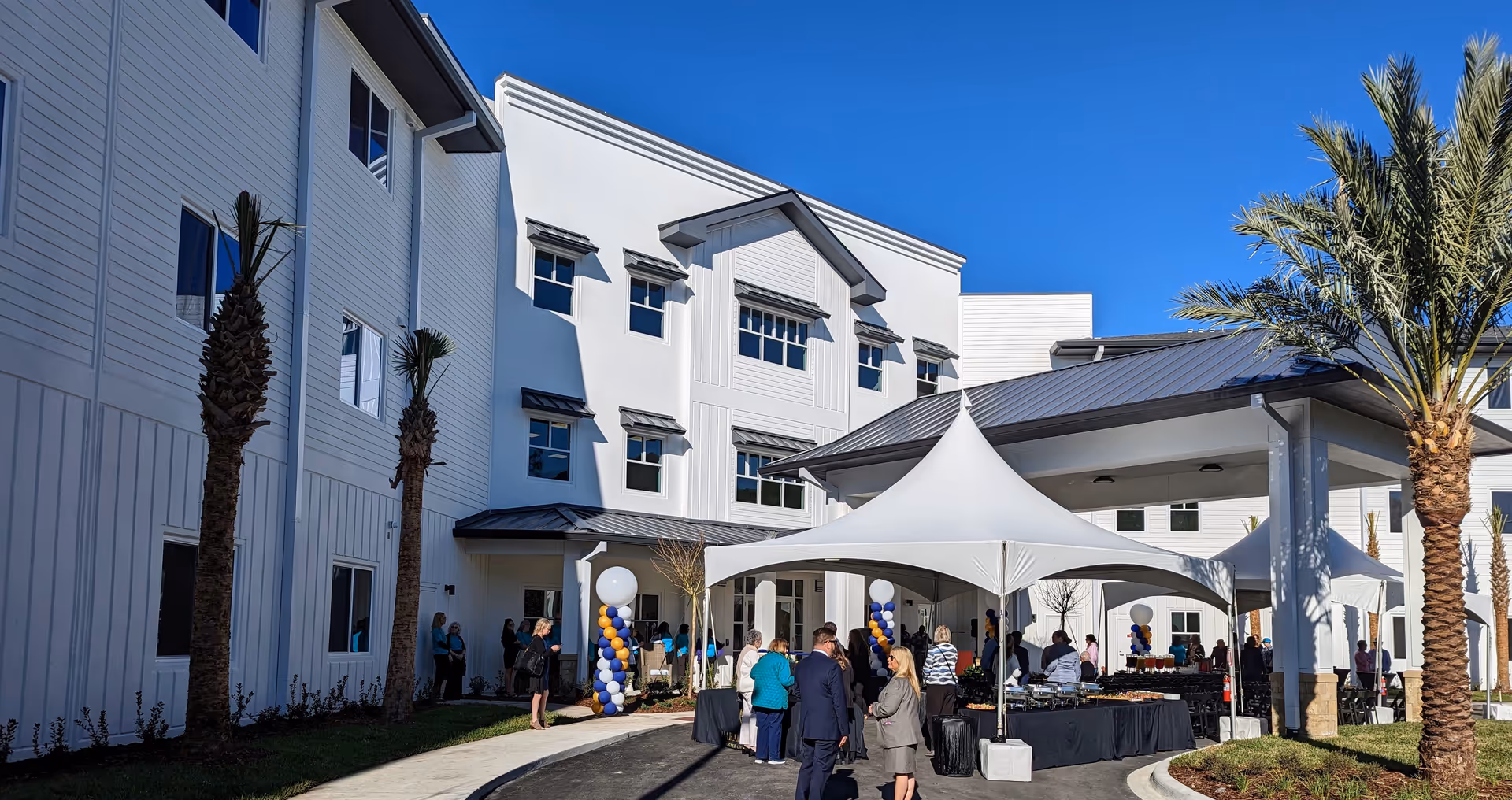 Exterior view of a white senior living facility with an outdoor event under canopies.