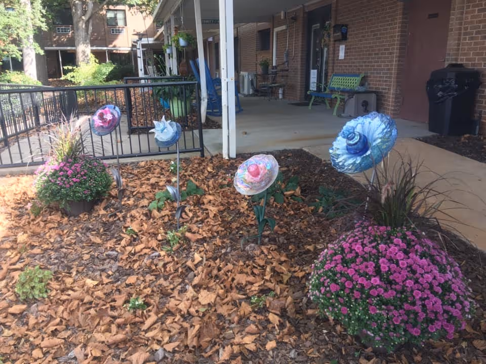 Outdoor courtyard with mulch, potted flowers, decorative garden ornaments, and a walkway near brick building.