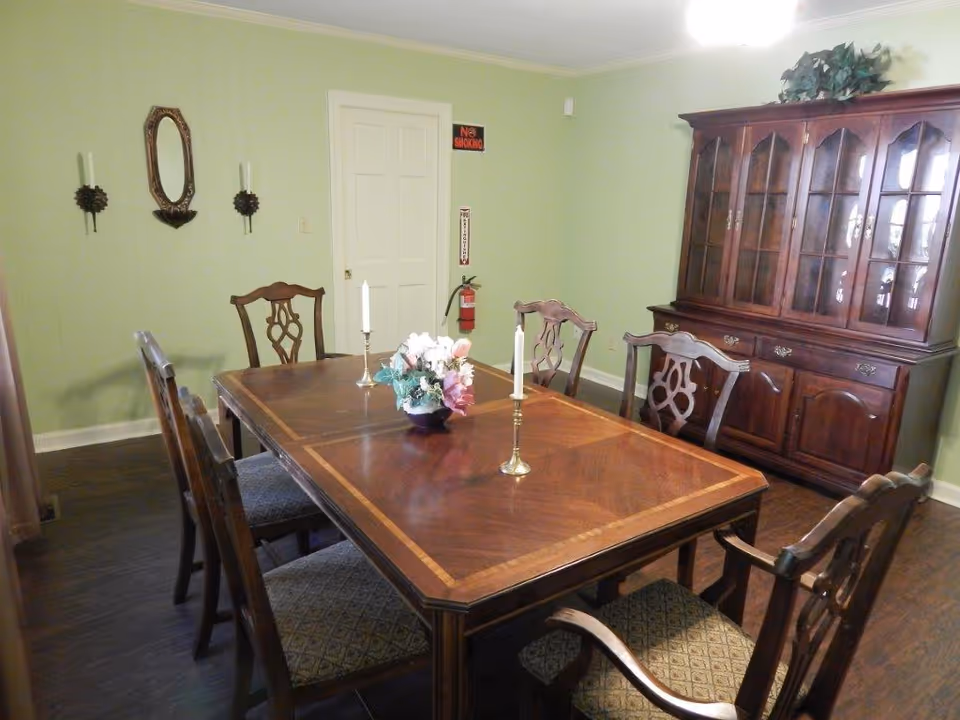 Green-walled dining room featuring a wooden table, chairs, and a china cabinet.