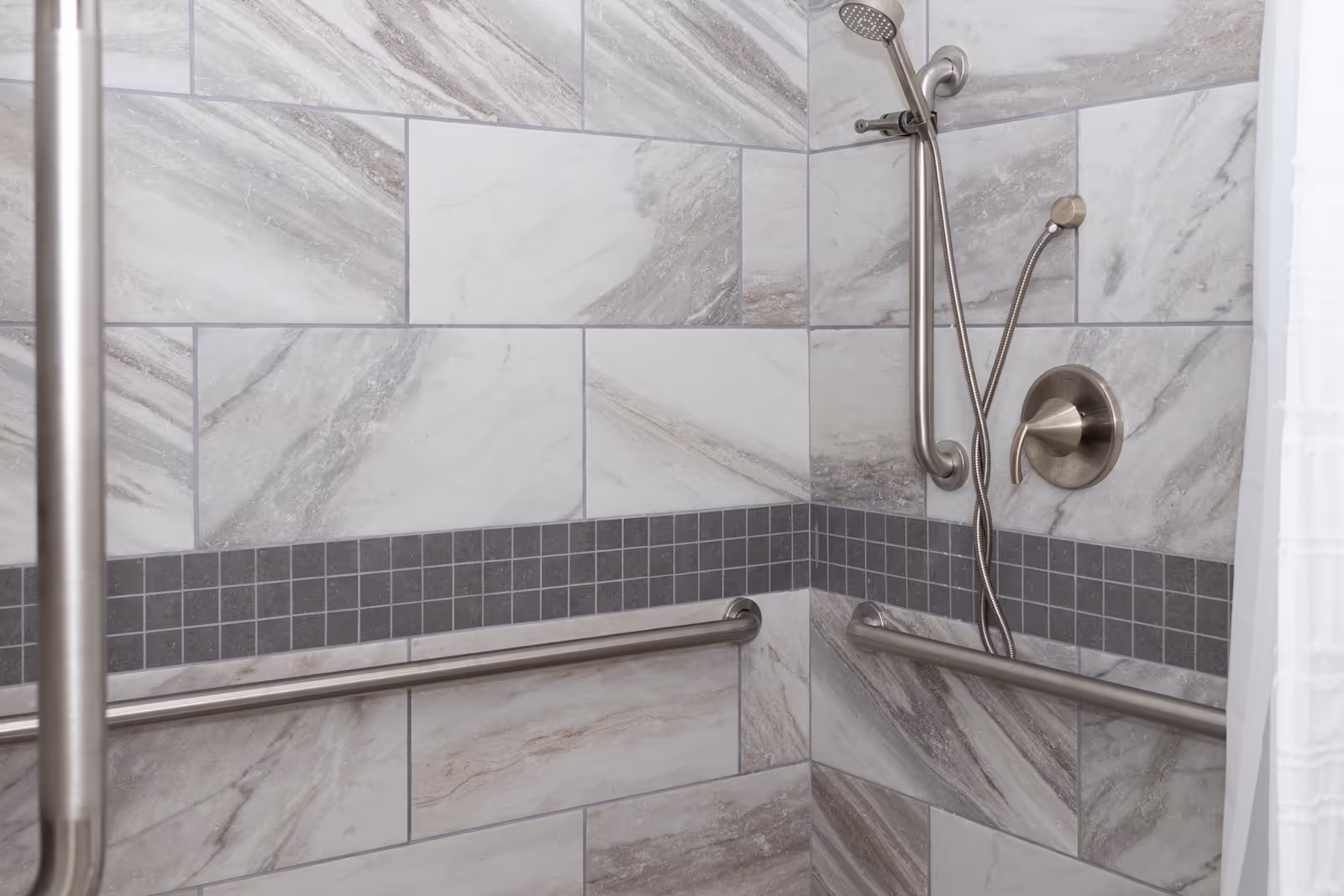 Accessible tiled bathroom shower with dual grab bars and handheld shower.
