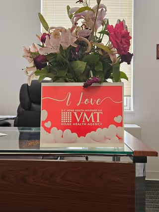 Desk with a bouquet and a VMTHC Home Health Agency sign in a bright reception area.