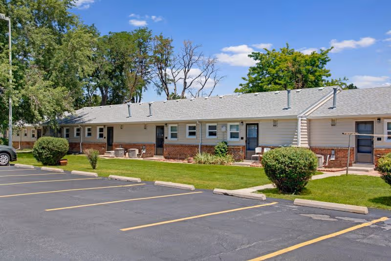 Single-story senior living facility exterior with parking lot, lawn and shrubs