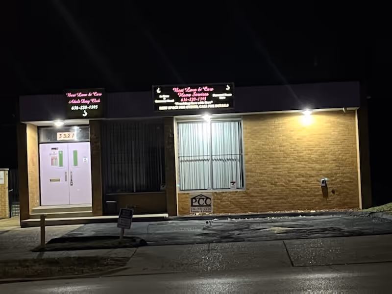 Night exterior of a brick facility with illuminated signs and a purple front door.