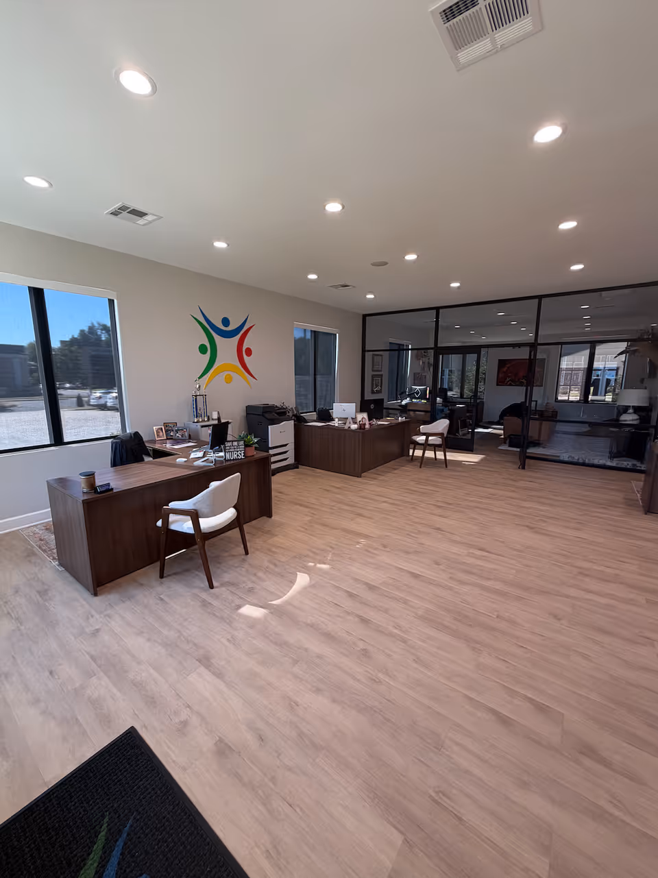 Modern lobby area with desks, glass partition, and a colorful multi-person logo on wall.