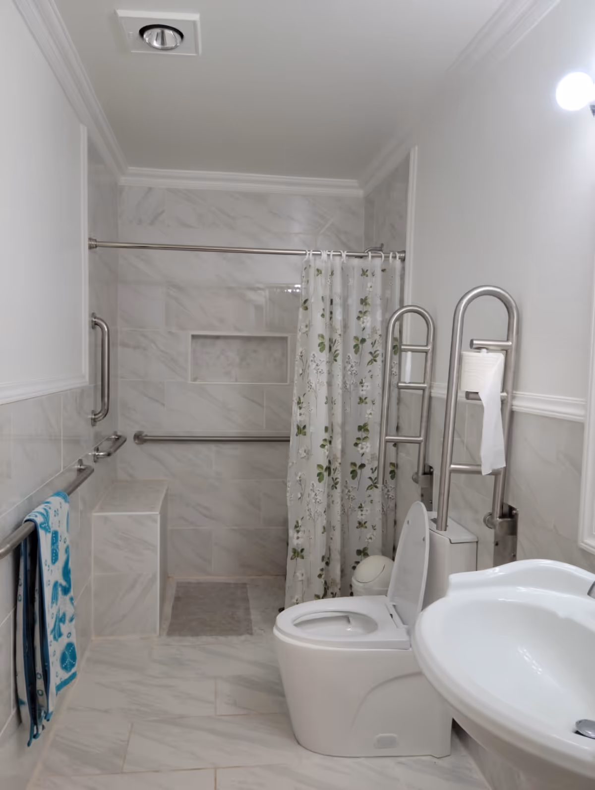 Accessible bathroom with walk-in shower, bench, grab bars, toilet, sink, and shower curtain.