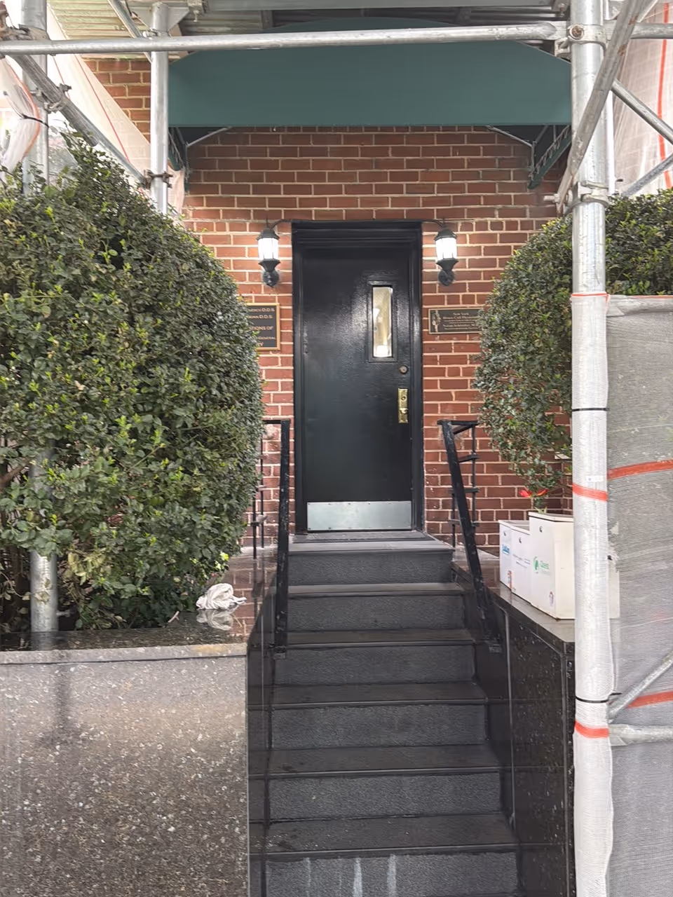 Brick building entrance with green awning, black door, and scaffolding.