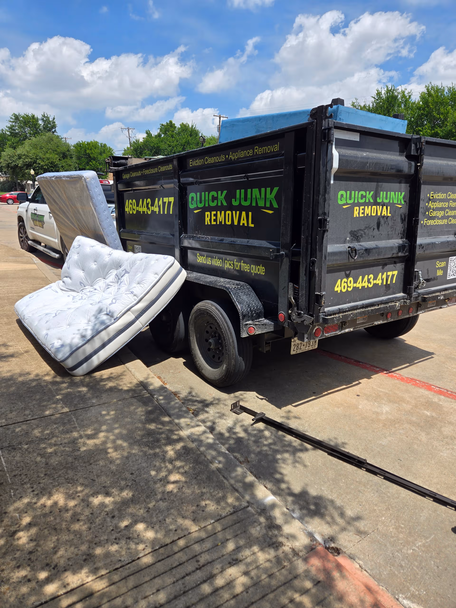 A junk removal truck with a mattress leaning against it in a parking lot.