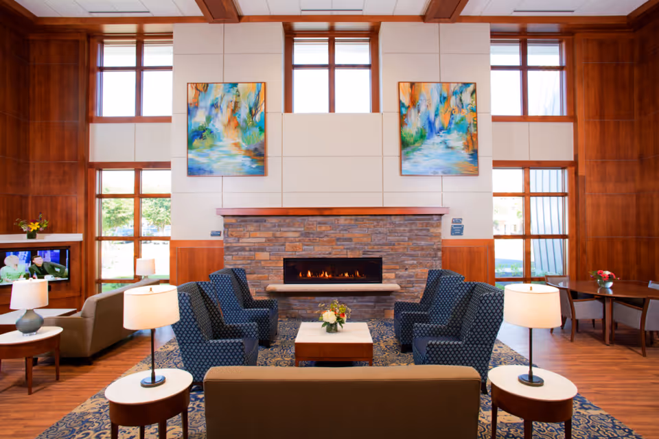Elegant lounge area with a stone fireplace, blue armchairs, tables, and large windows.