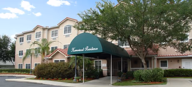 Exterior view of a beige senior living building with a green entrance canopy and landscaping.