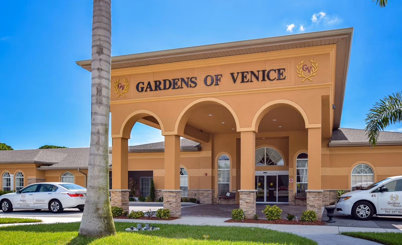 Exterior view of Gardens of Venice facility entrance with arches and parked cars.