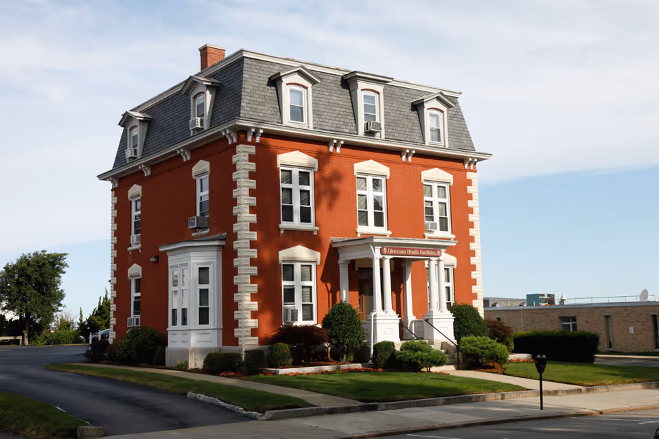Red brick, three-story building with white trim and a covered front entrance.