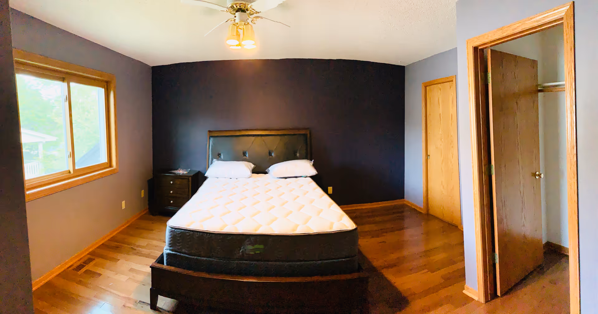Bedroom with a queen bed, dark accent wall, window, ceiling fan, and closet.