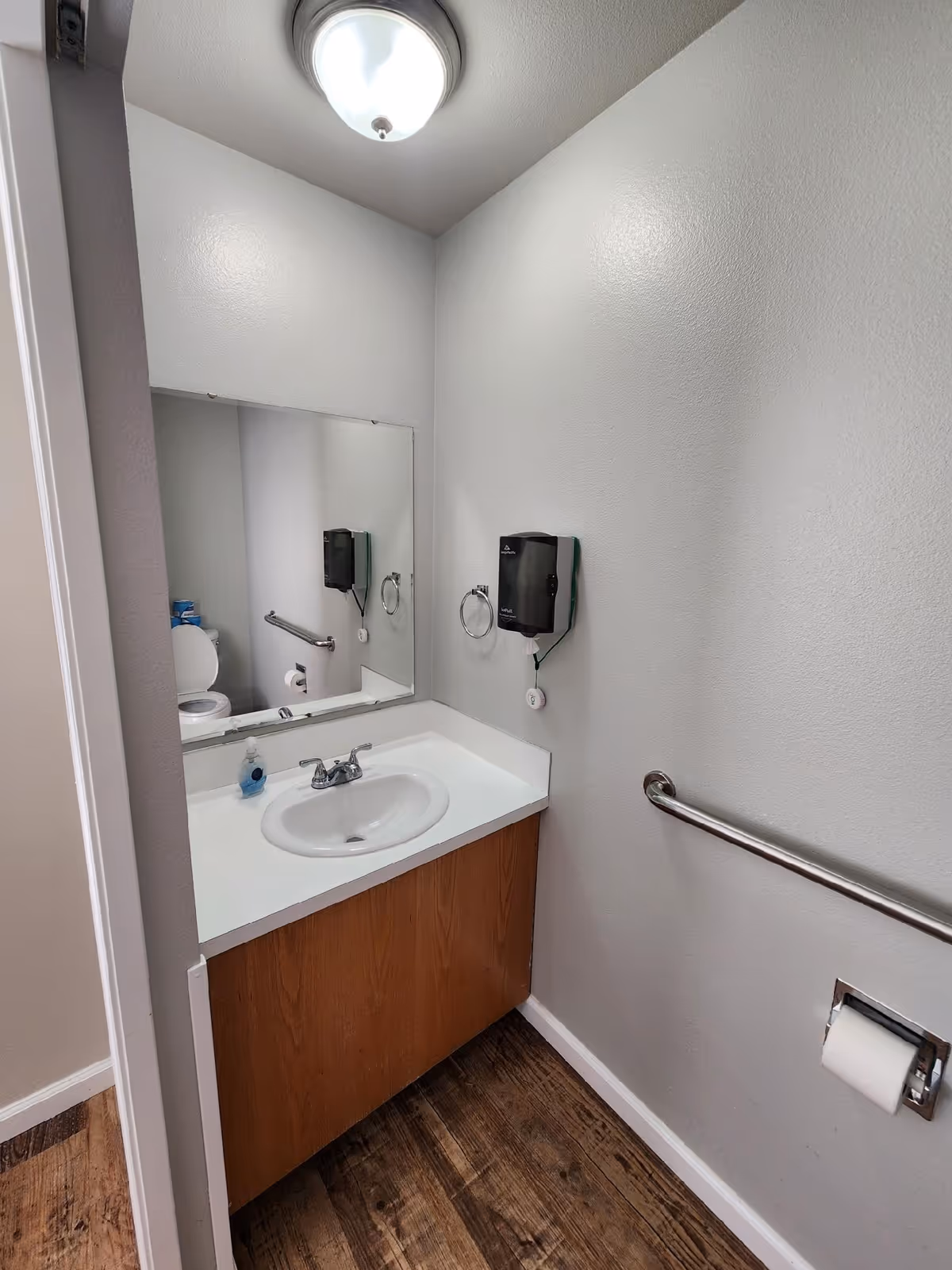 Small bathroom with sink, mirror, toilet in reflection, and wall grab bar.