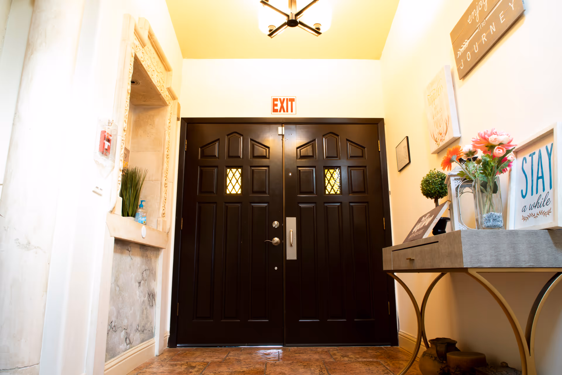 Interior foyer featuring dark double doors, an EXIT sign, and a decorative table with flowers.