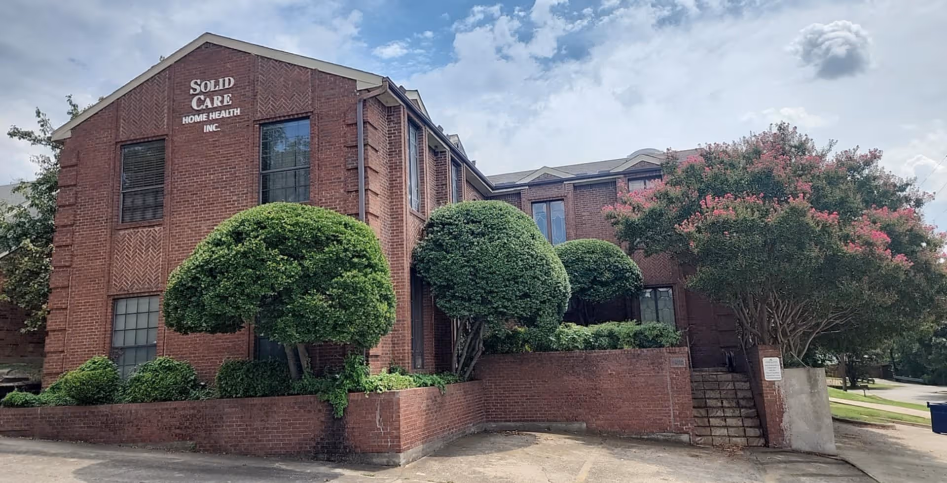 Brick building front of Solid Care Home Health Inc with trimmed trees.
