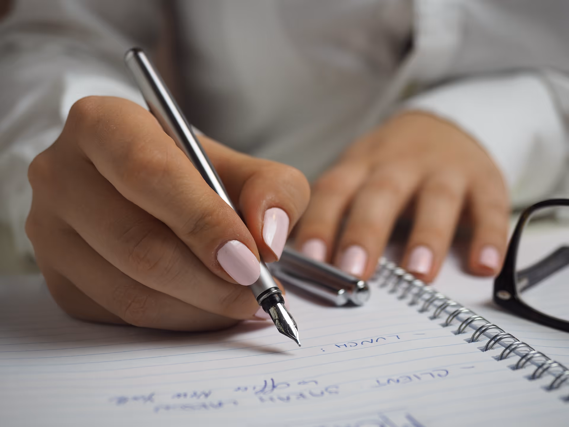 Close-up of a hand writing with a pen in a spiral notebook.