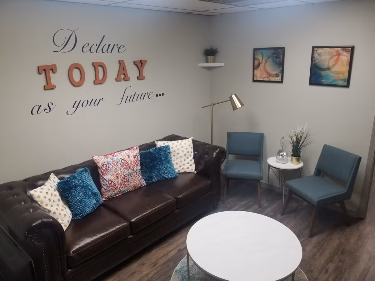 Cozy waiting area with leather sofa, blue chairs, round marble table, and wall art.