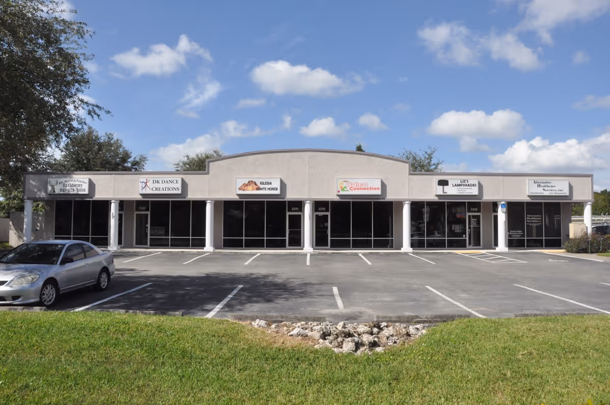 Front view of a strip mall with multiple storefronts, parking lot, and clear blue sky.